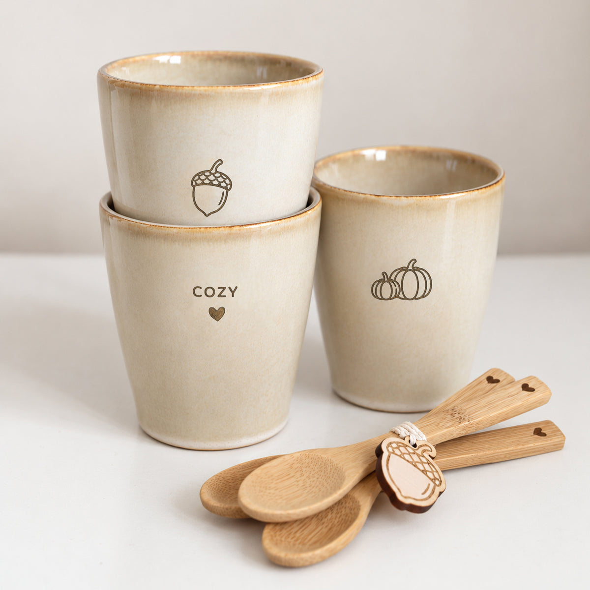 Drie beige gegraveerde herfst koffiemokken met eikeltje, pompoentjes en Cozy Season met bamboelepeltjes.