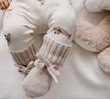 baby met handgemaakte jongenskleding met bruine print en beige slofjes van wol