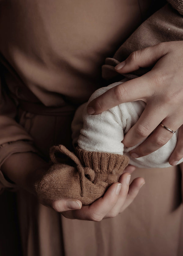 handen die newborn baby vasthouden met badstof broekje en wollen slofjes